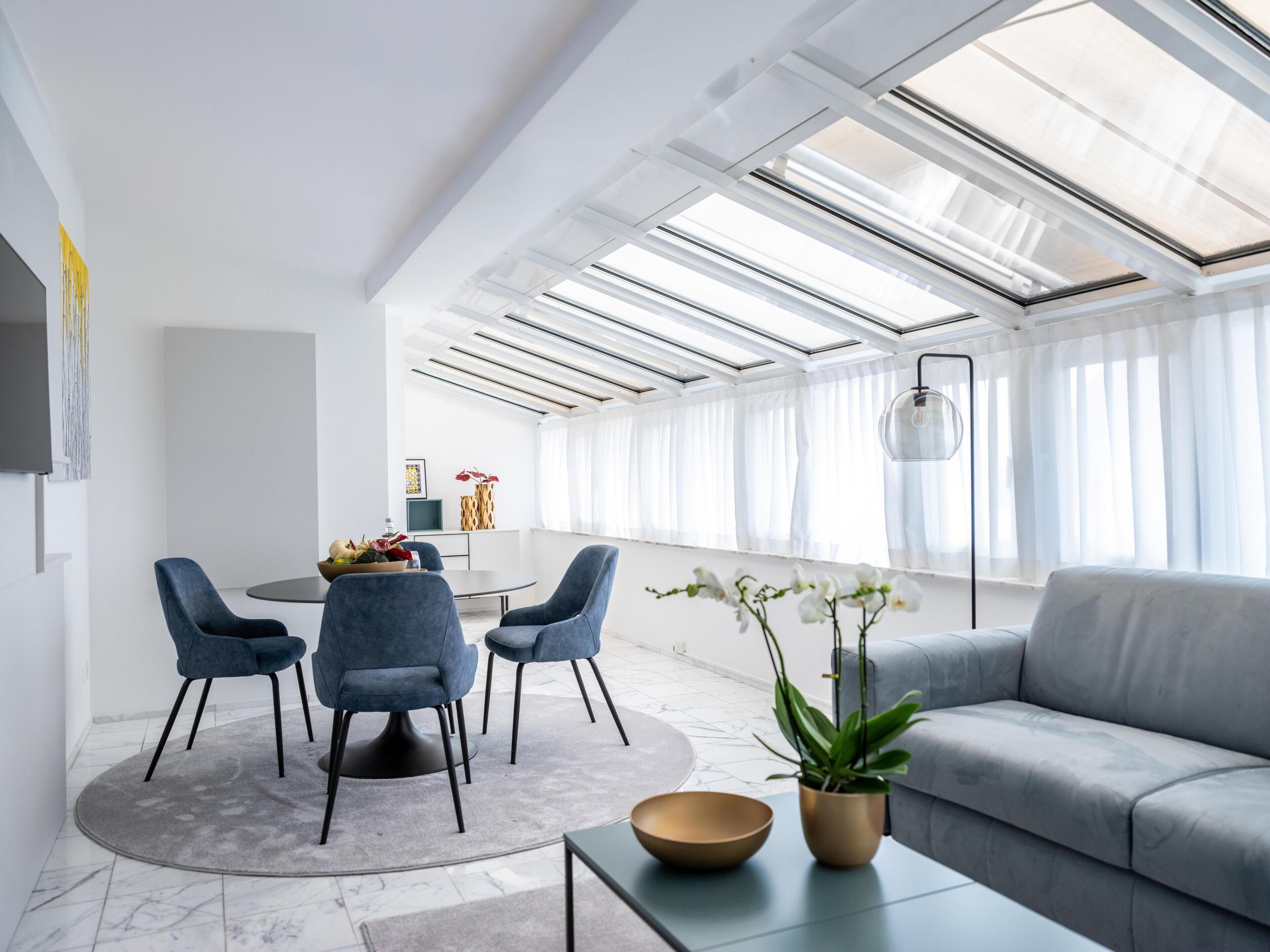 A modern living room with a sofa, chairs, a dining table, and a large window with natural light.