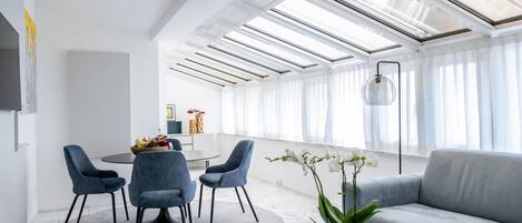 A modern living room with a sofa, chairs, a dining table, and a large window with natural light.
