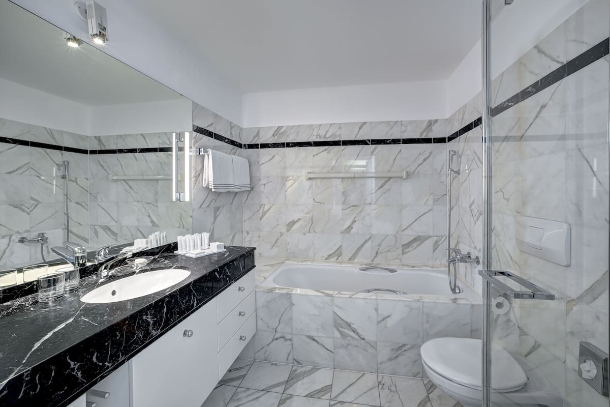 Un baño moderno con lavamanos de mármol negro, inodoro blanco y zona de ducha con mampara de cristal.