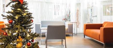 A modern living room with a Christmas tree, a grey armchair, and an orange sofa.