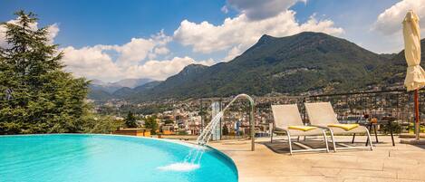 A swimming pool with a water feature, lounge chairs, and a view of a mountainous landscape.