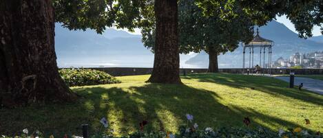 A park with large trees, a gazebo, and a view of a body of water and mountains.