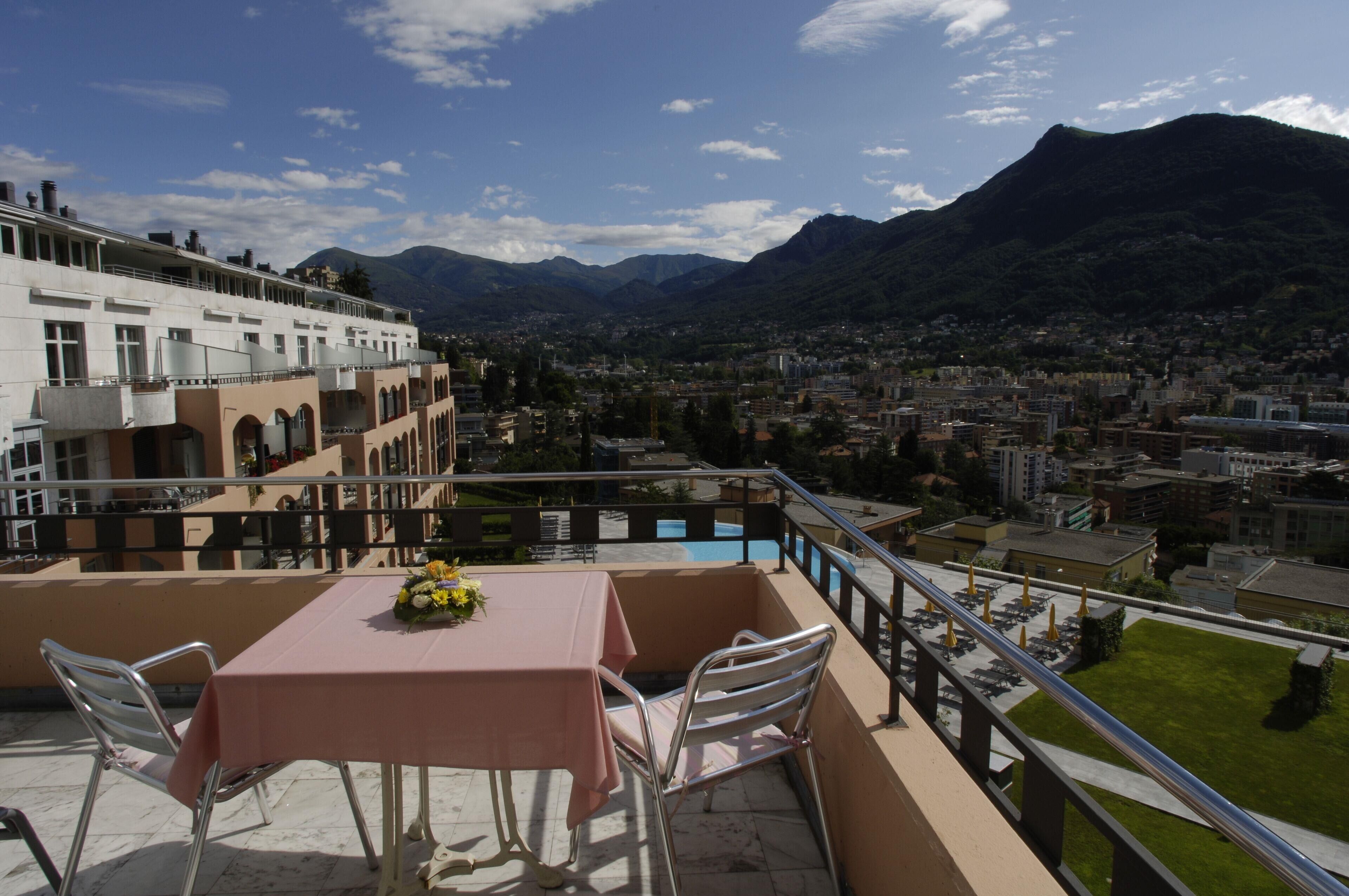 A balcony with a table and chairs, overlooking a cityscape and mountains.