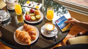 Una mesa de desayuno con croissants, fruta, jugo, café y un libro.
