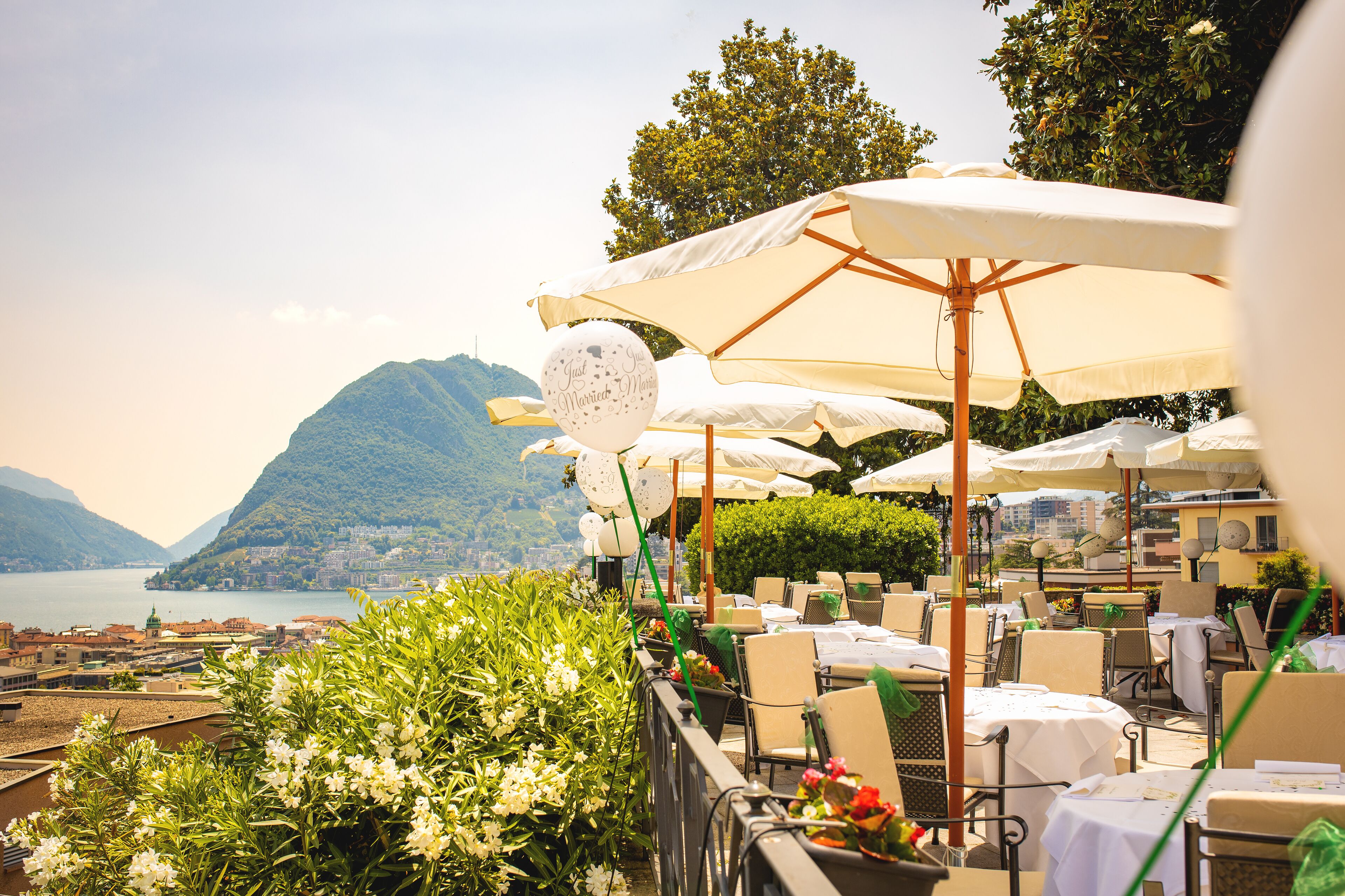 An outdoor dining area with tables and chairs, umbrellas, and a scenic view of a lake and mountains.