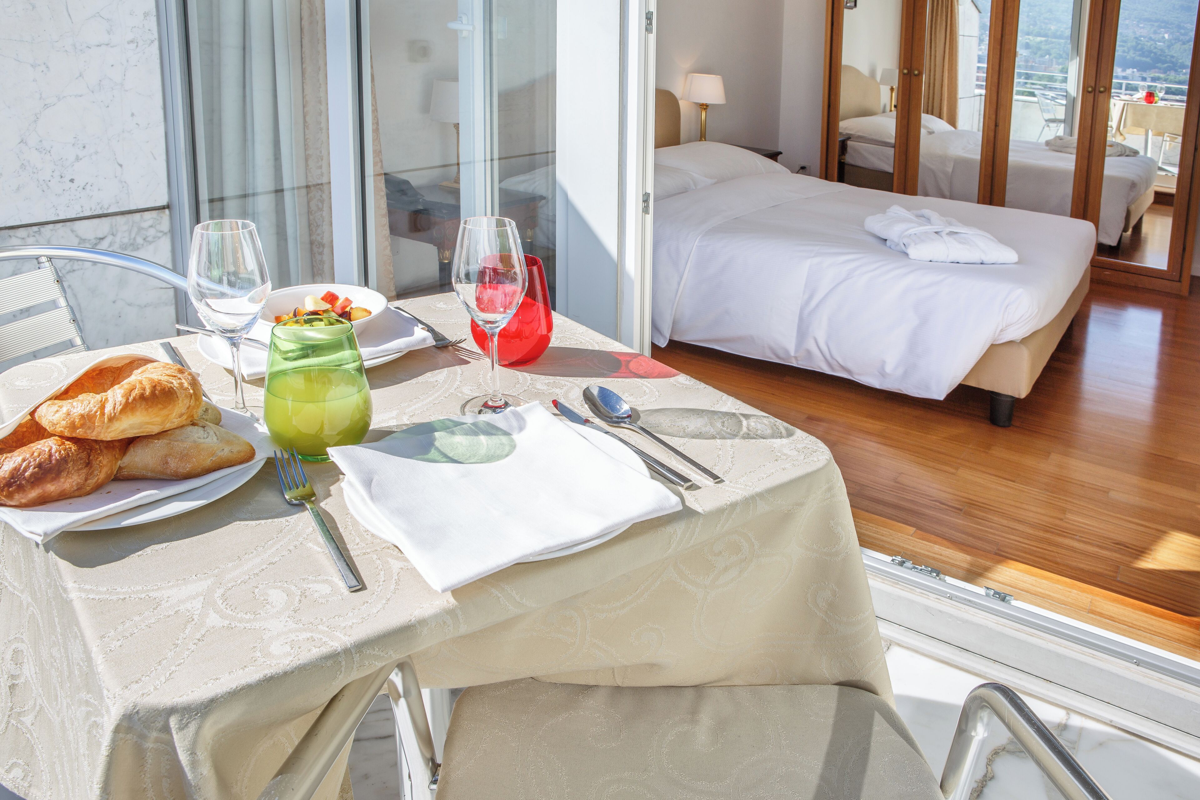 Ein Hotelzimmer mit einem Bett, einem Esstisch mit Frühstück und Blick auf die Stadt.