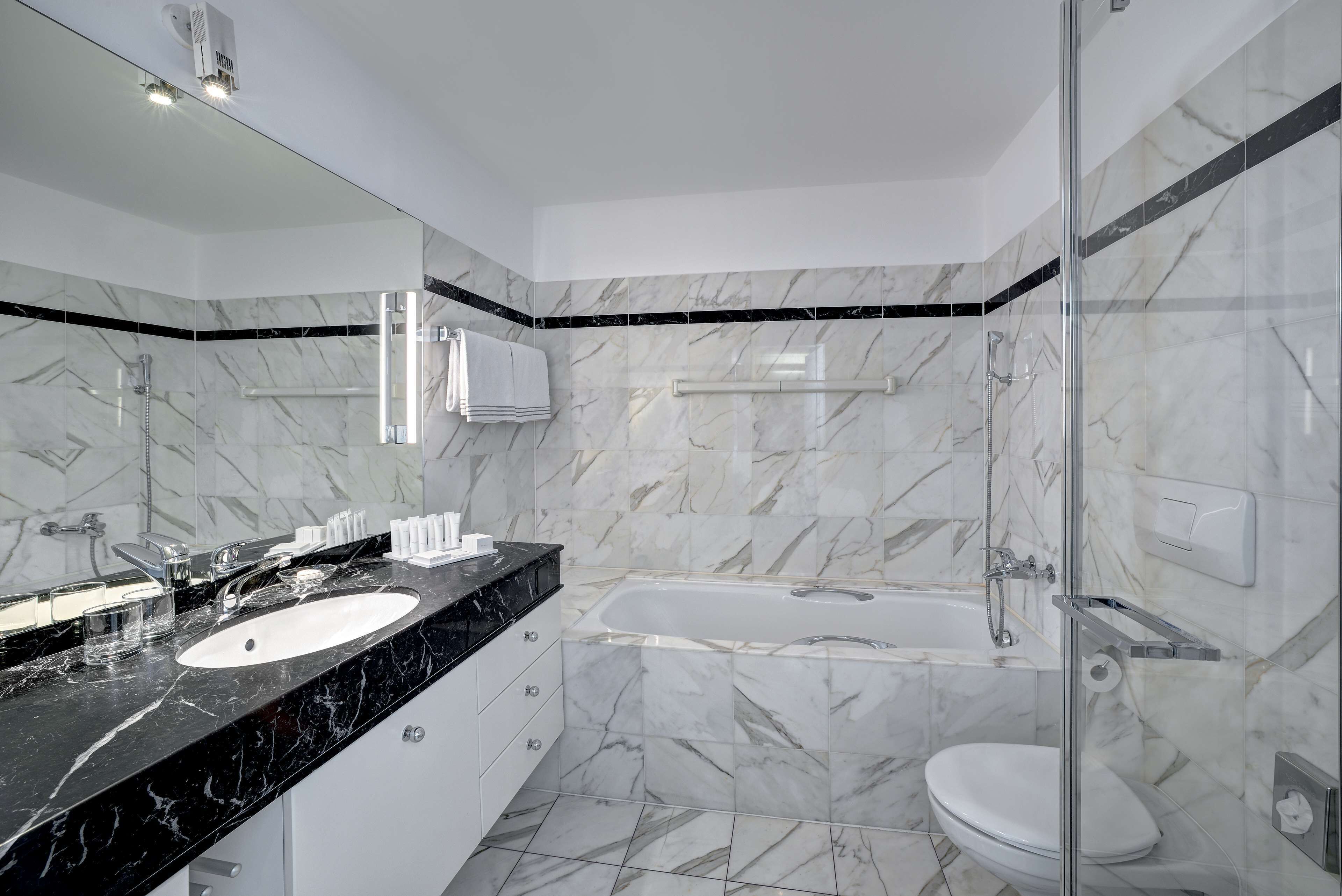 A modern bathroom with a black marble countertop, a white sink, a glass-enclosed shower, and a white toilet.