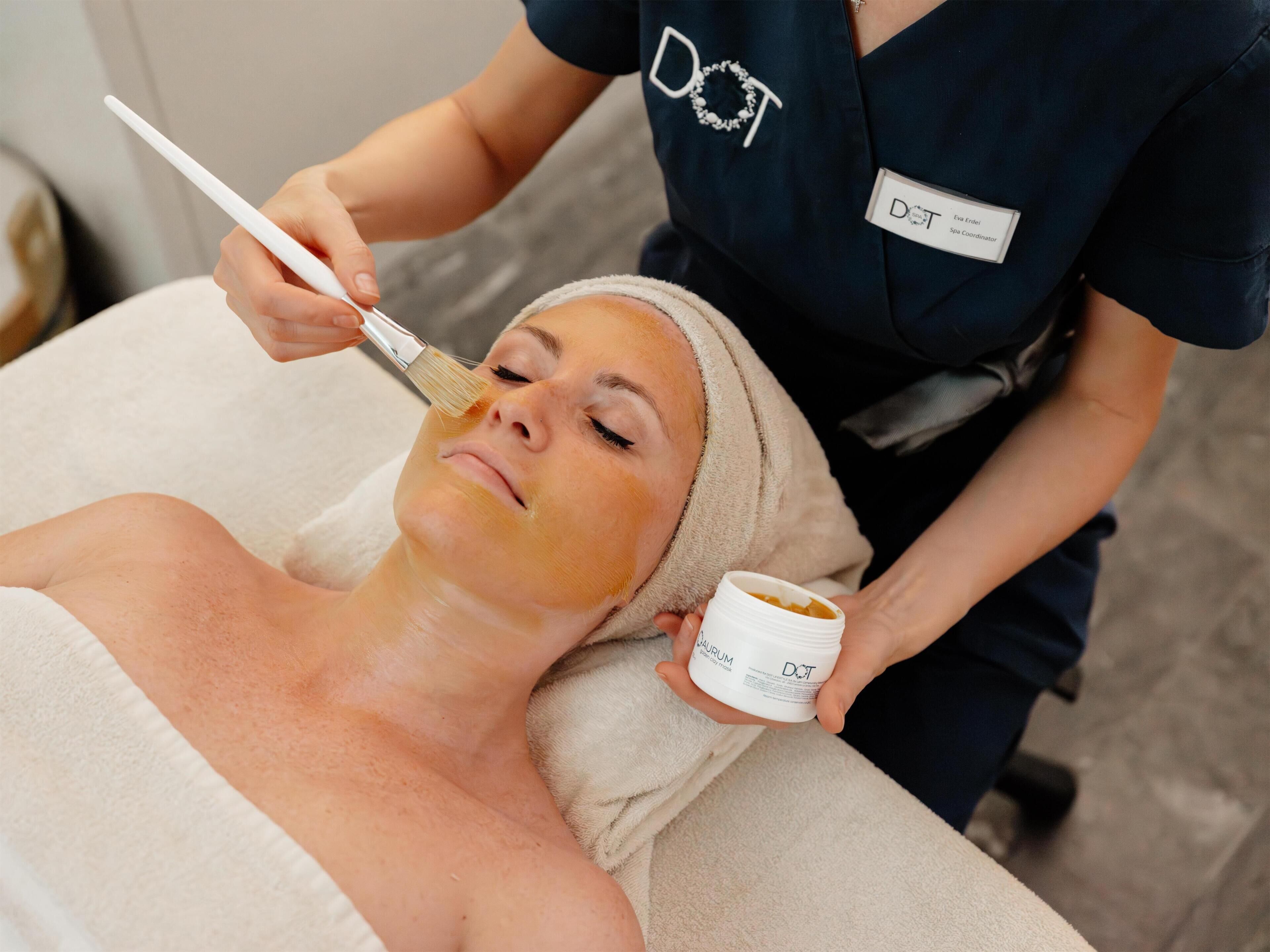 A person receiving a facial treatment with a brush and a jar of cream.