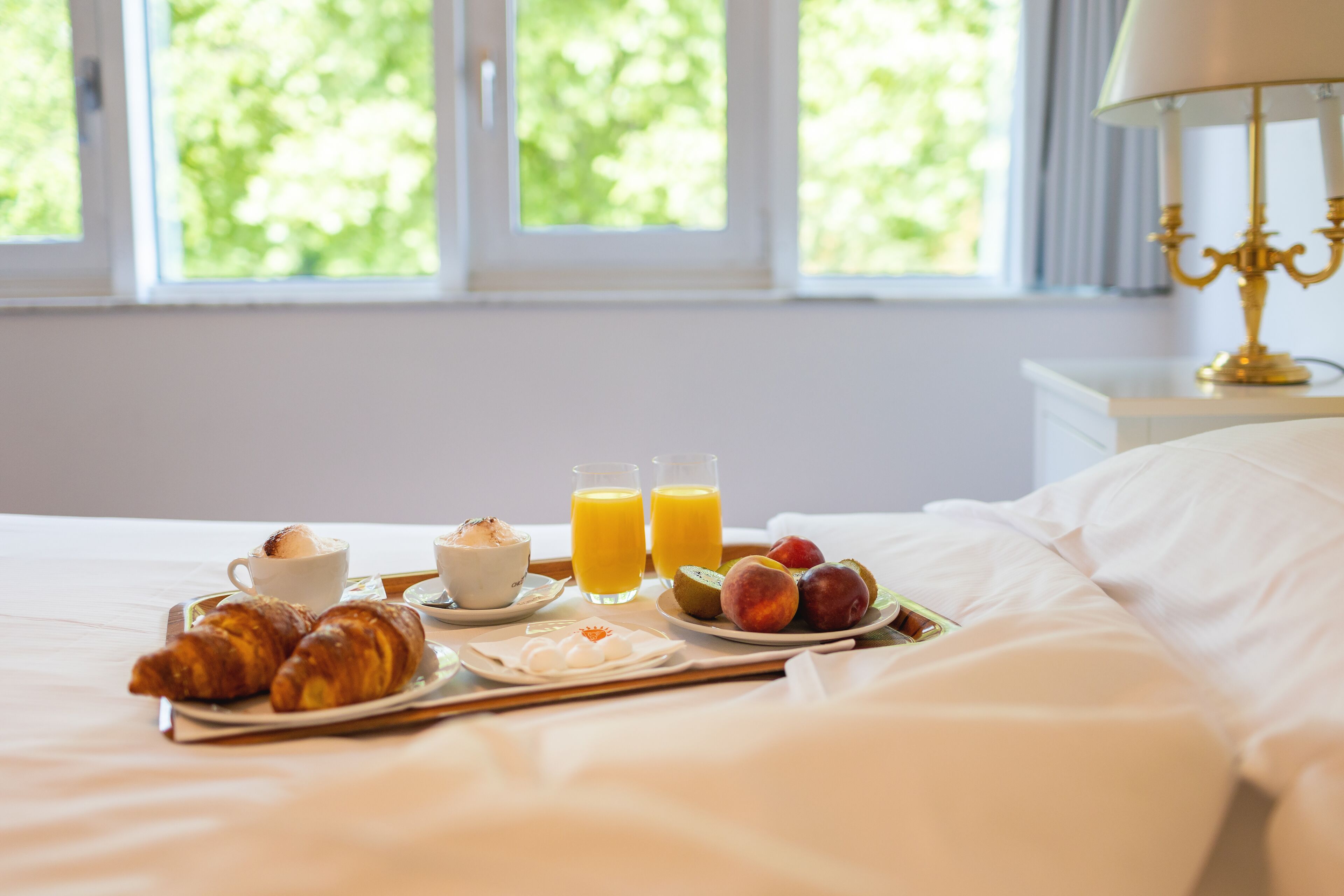 A breakfast tray with croissants, fruit, and orange juice on a bed with white linens.