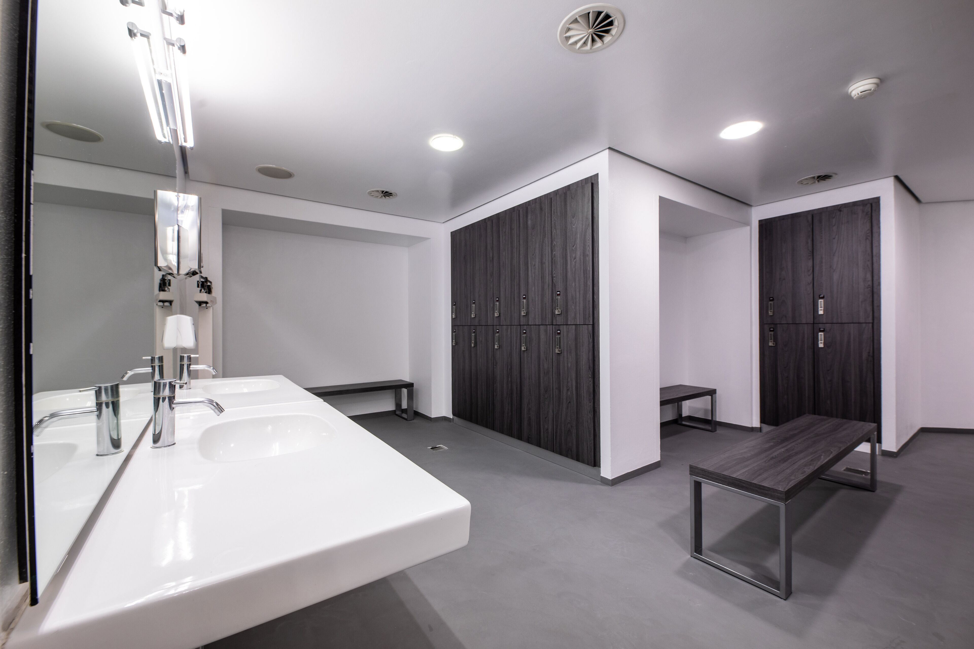 A modern bathroom with two sinks, a bench, and lockers.