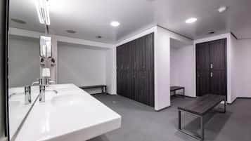 A modern bathroom with two sinks, a bench, and lockers.