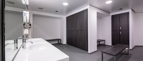 Un baño moderno con dos lavamanos, un banco y taquillas.