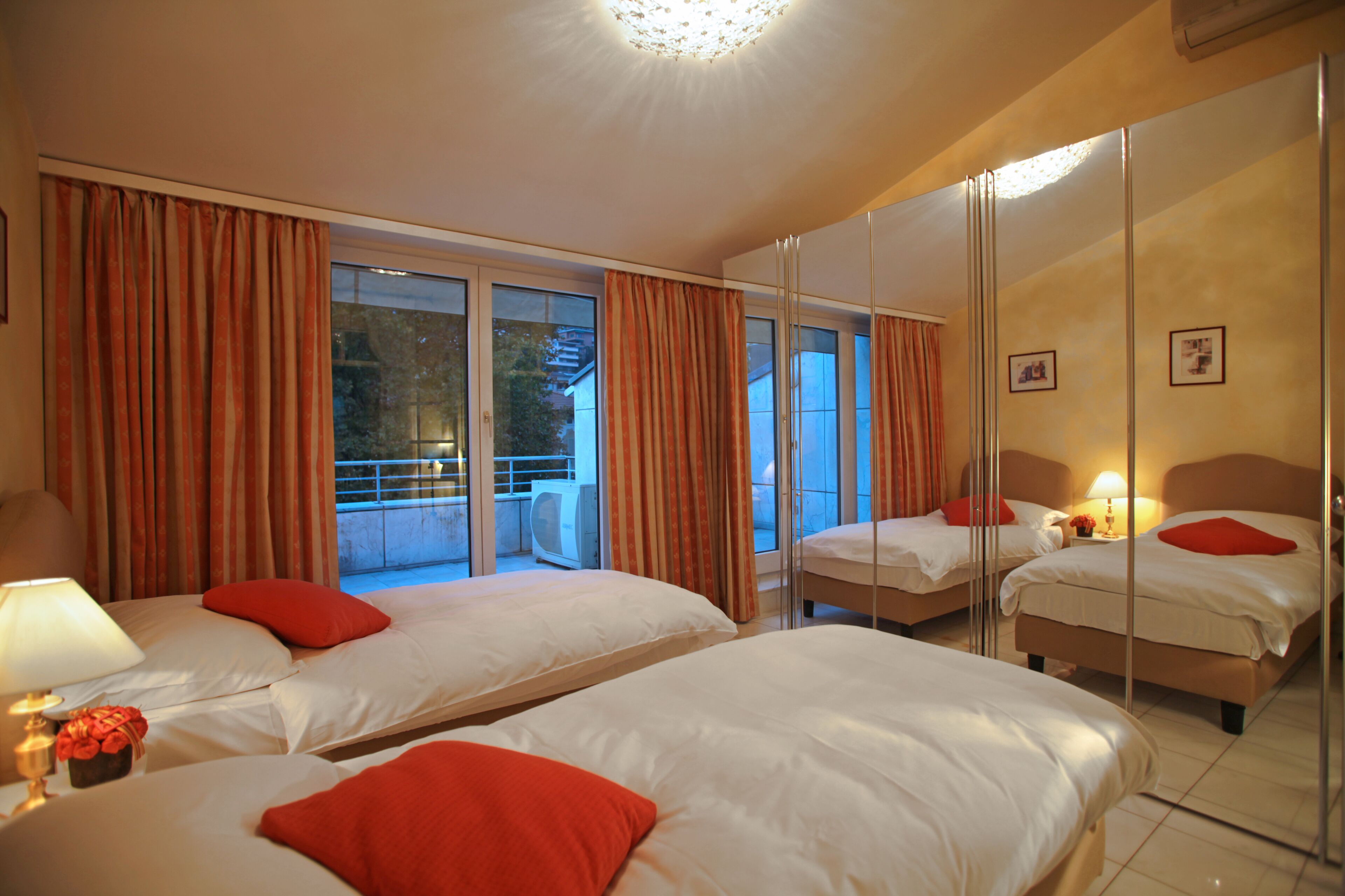 A hotel room with two beds, a large mirror, and a balcony with curtains.