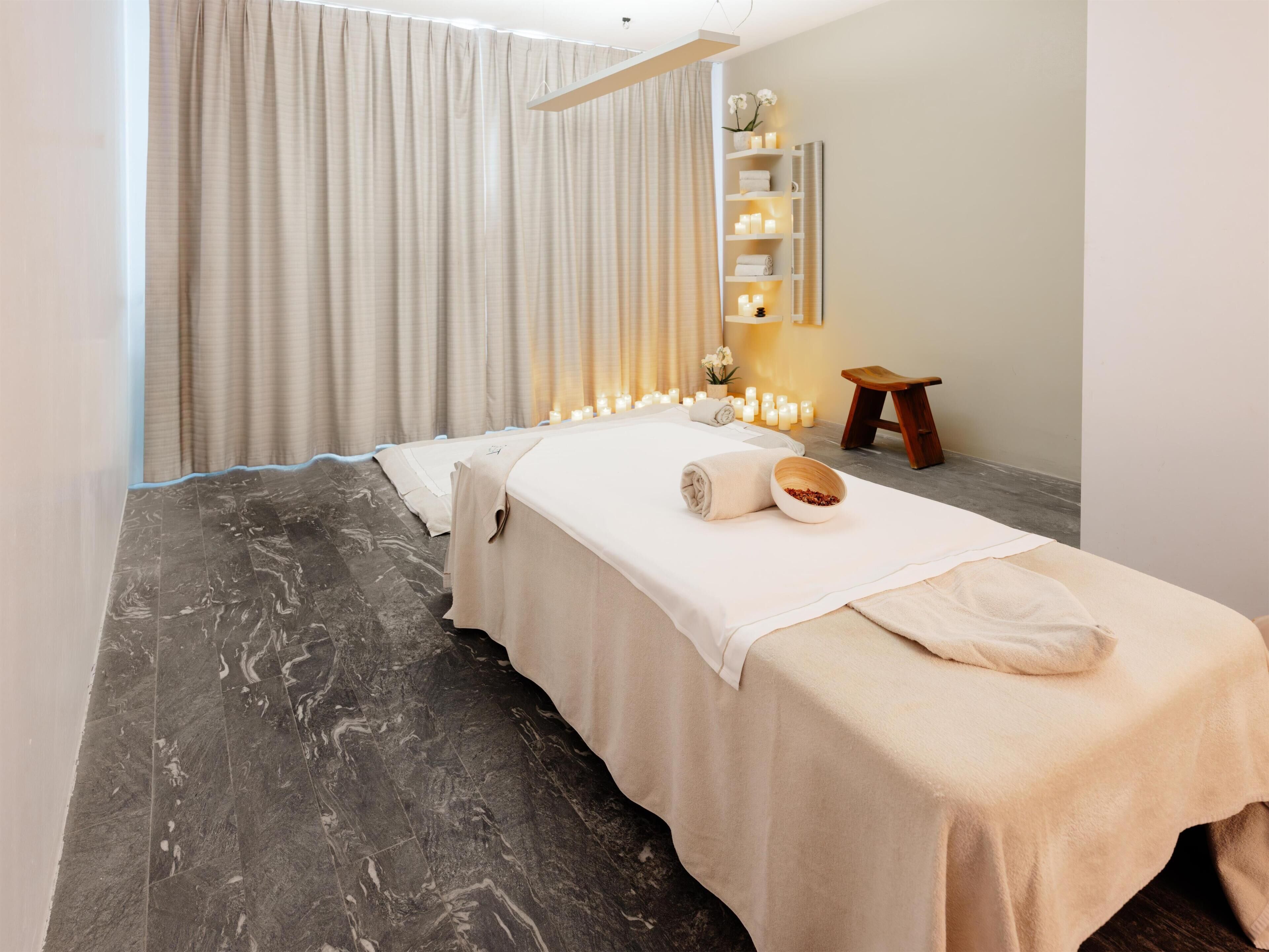 Une salle de spa équipée d’une table de massage, de bougies et d’un petit tabouret en bois.