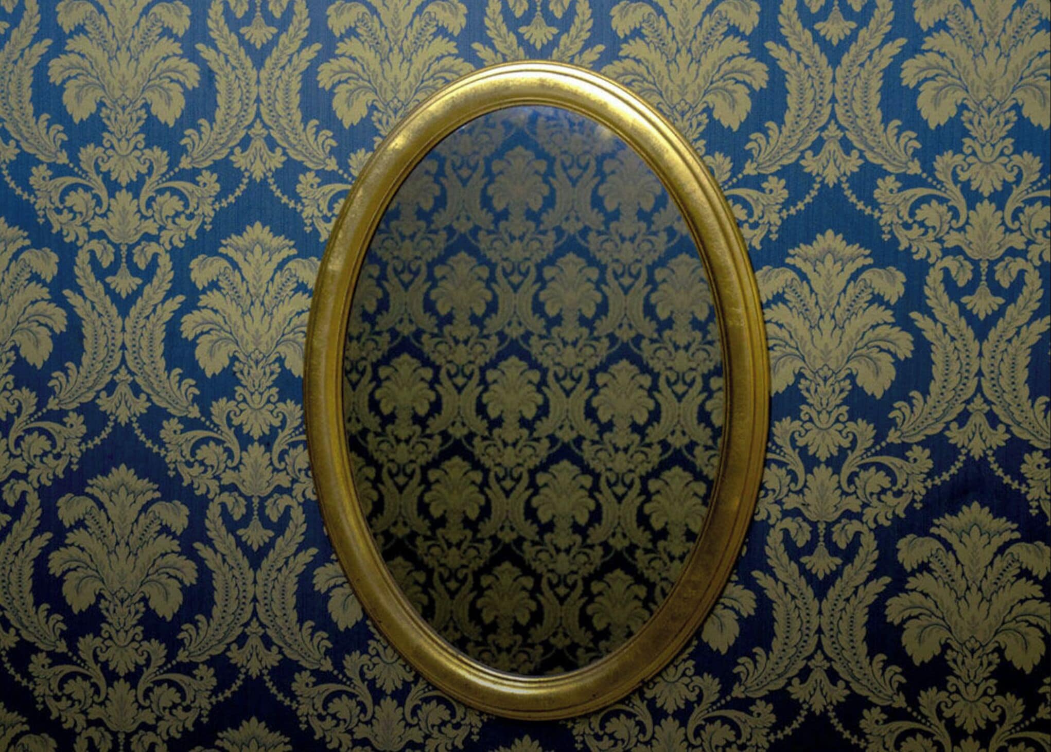 A mirror with a gold frame on a blue patterned wallpaper.