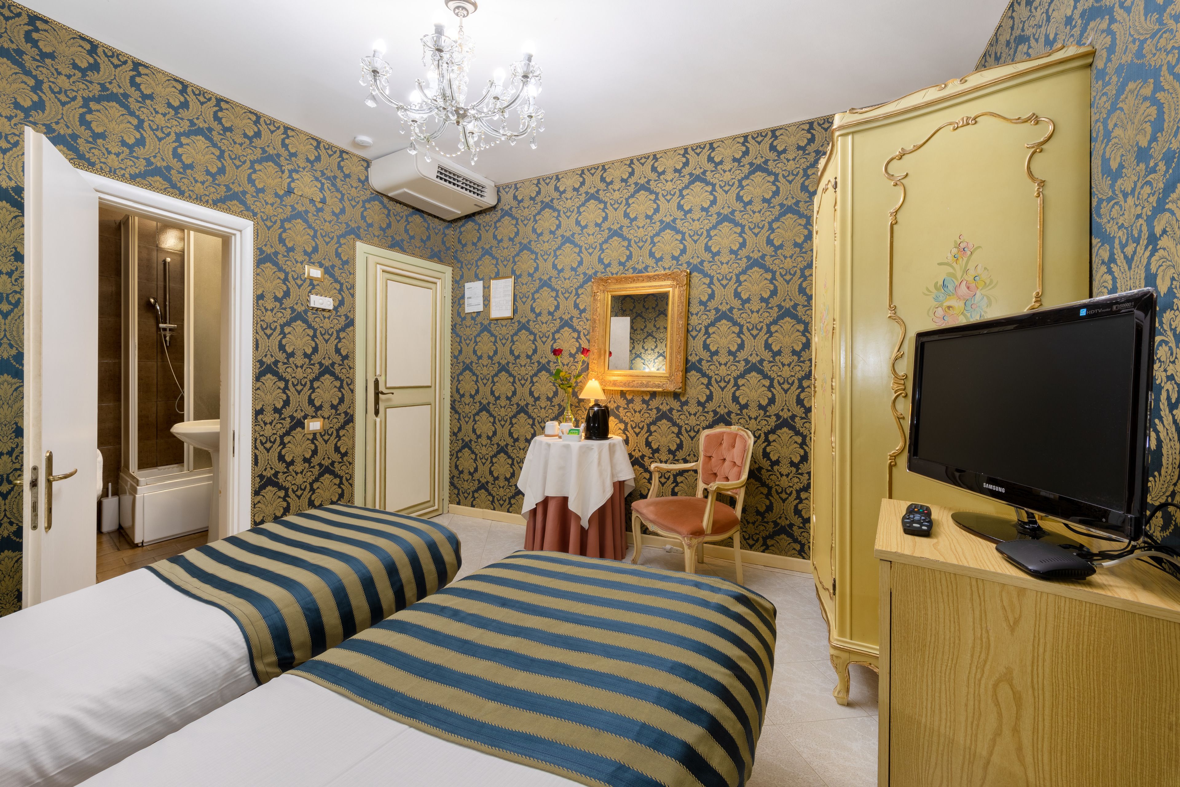 Habitación de hotel con dos camas, televisor, una silla y una mesa con un florero.