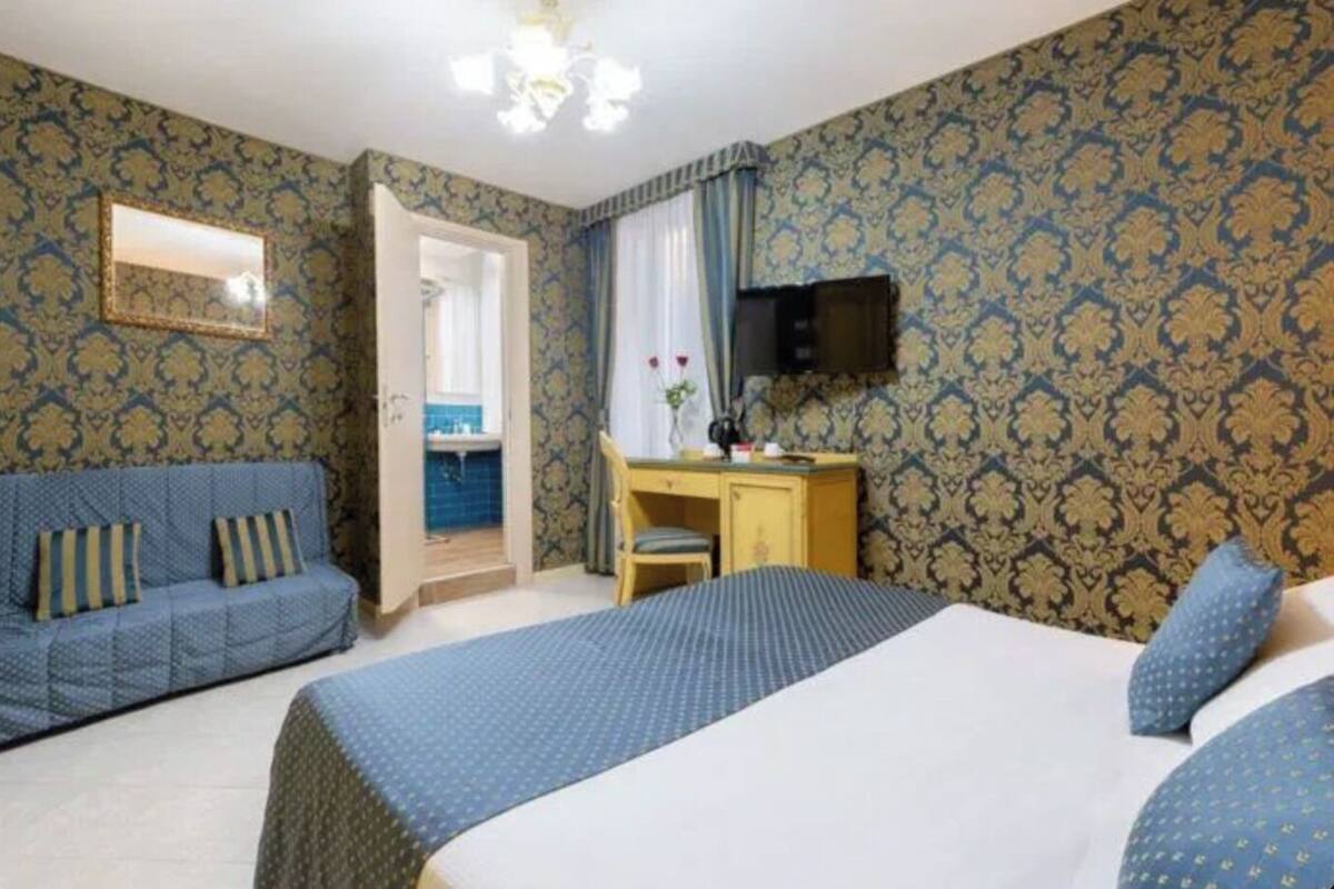 A hotel room with a bed, a desk, a chair, a sofa, and a television.