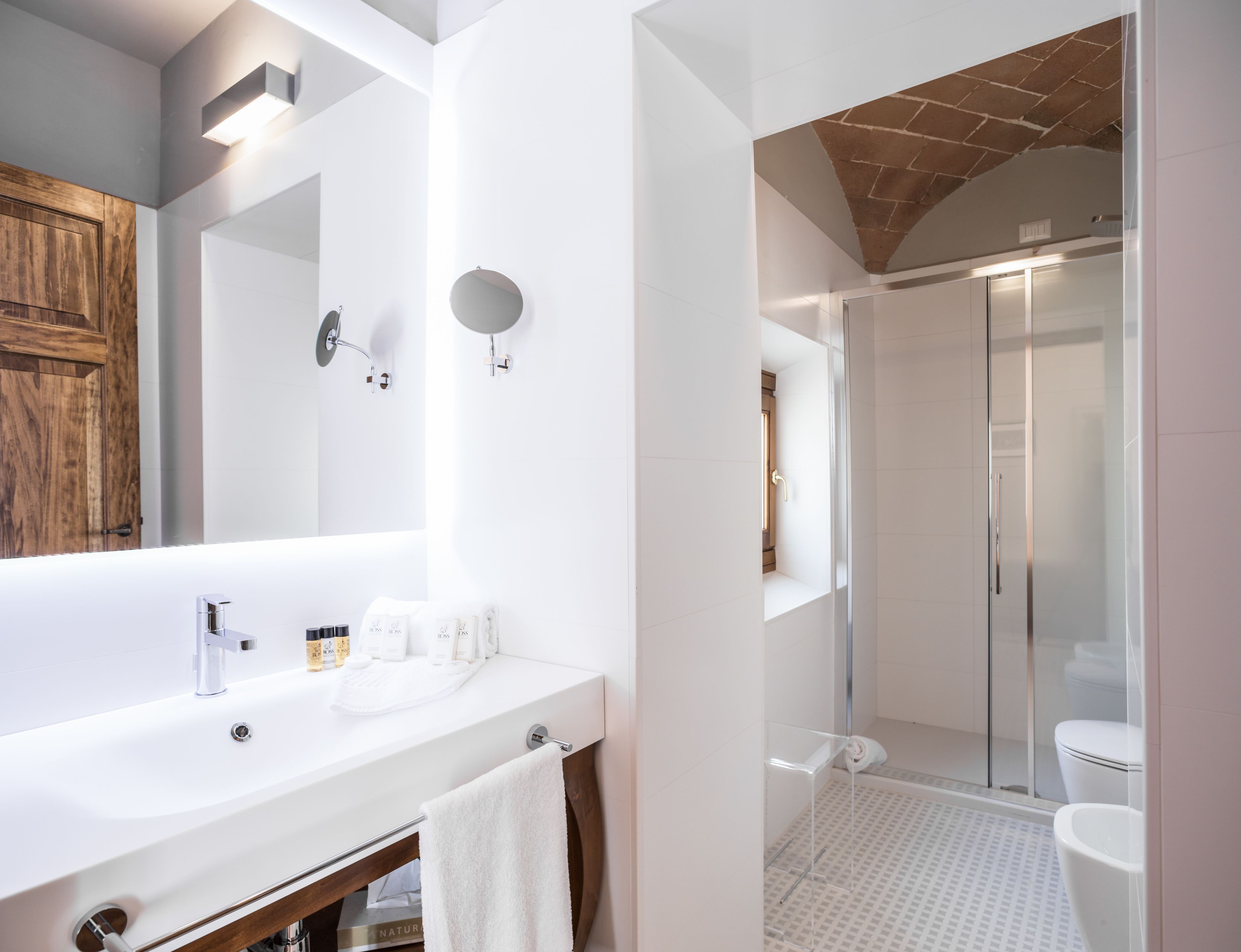 A modern bathroom with a large mirror, a white sink, and a glass-enclosed shower.
