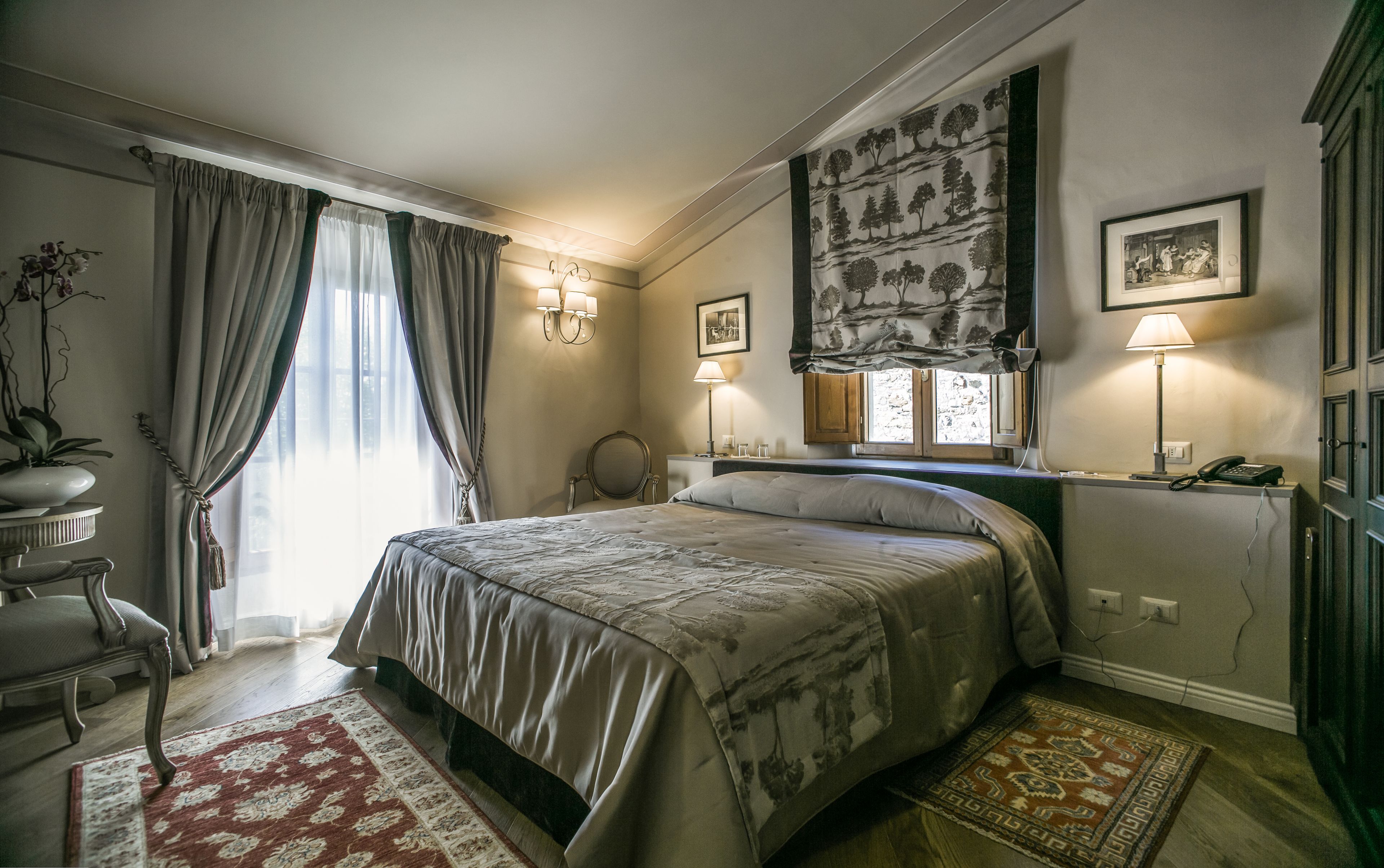 A well-lit bedroom with a large bed, a desk, a chair, a mirror, and two wall-mounted lamps.