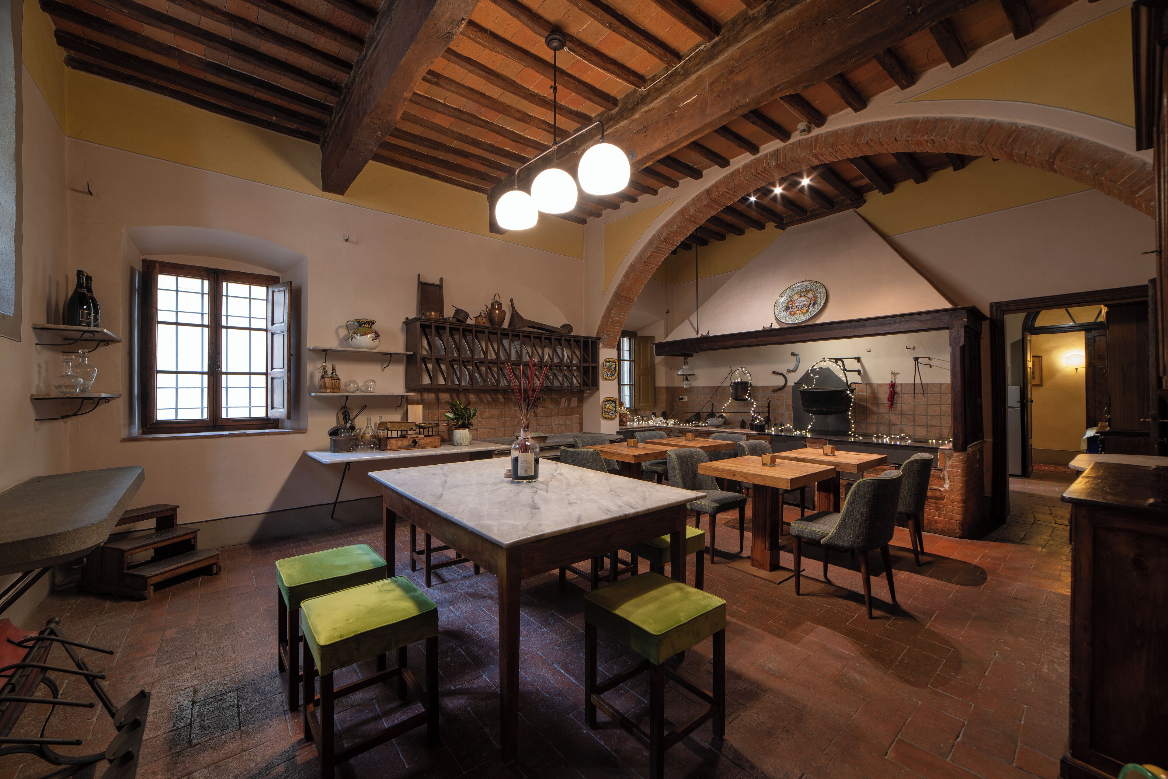 A rustic dining area with wooden tables and benches, a large window, and a brick oven in the background.