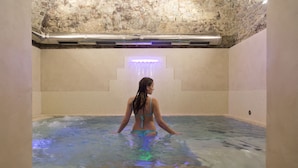 A woman in a blue bikini in a spa pool with a stone wall and a blue light fixture. - Palazzo Leopoldo Dimora Storica & Spa (Radda in Chianti)
