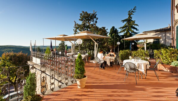 An outdoor patio with tables and chairs, surrounded by potted plants and a railing. - Palazzo Leopoldo Dimora Storica & Spa (Radda in Chianti)