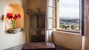 A room with a view of a valley, a stone shelf with flowers, a wooden bench, and a fireplace. - Palazzo Leopoldo Dimora Storica & Spa (Radda in Chianti)