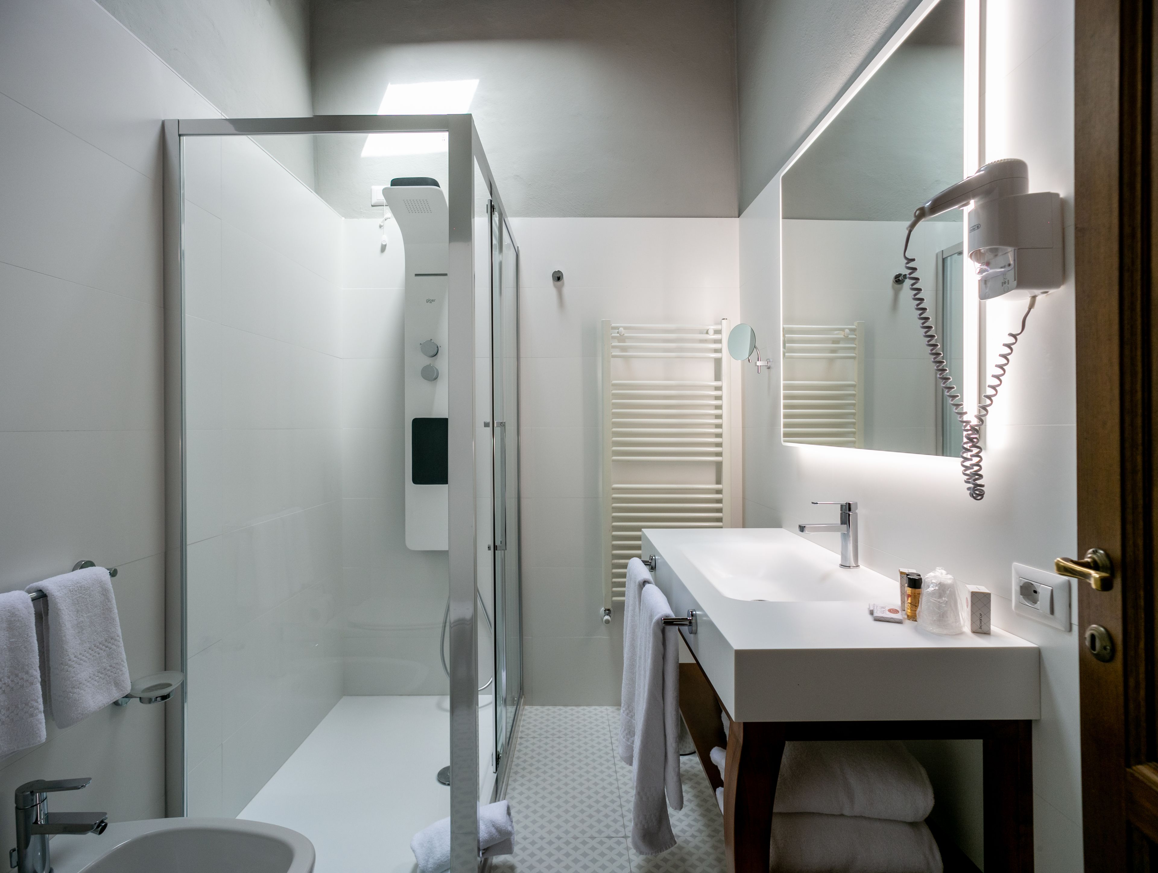 A modern bathroom with a glass shower enclosure, a white sink with a mirror, and a towel rack.