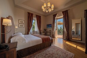 A hotel room with a large bed, a desk with a telephone, a chandelier, and a view of the outdoors through a door. - Palazzo Leopoldo Dimora Storica & Spa (Radda in Chianti)