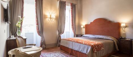 A bedroom with a wooden ceiling, a bed with a headboard, a nightstand, a desk with a chair, and a window with curtains.