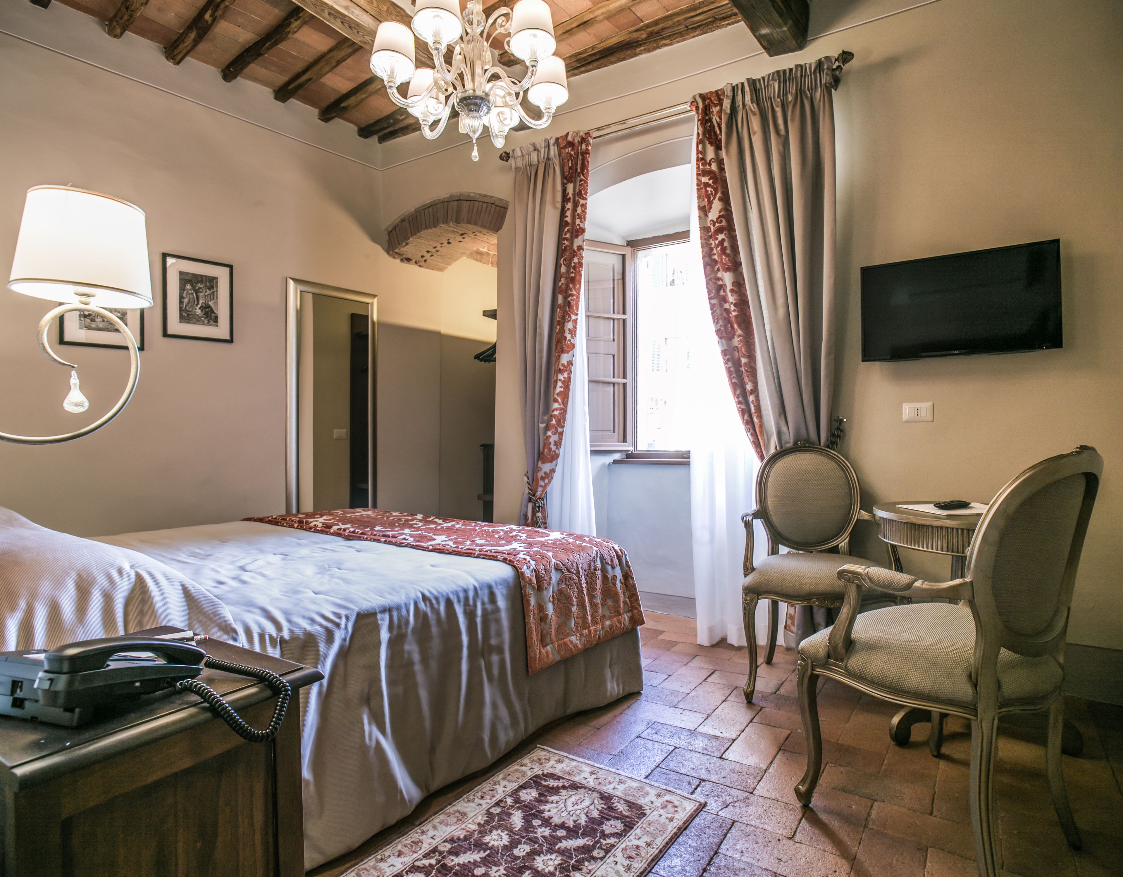 A hotel room with a bed, bedside lamp, telephone, chair, desk, television, and a view of the outside.