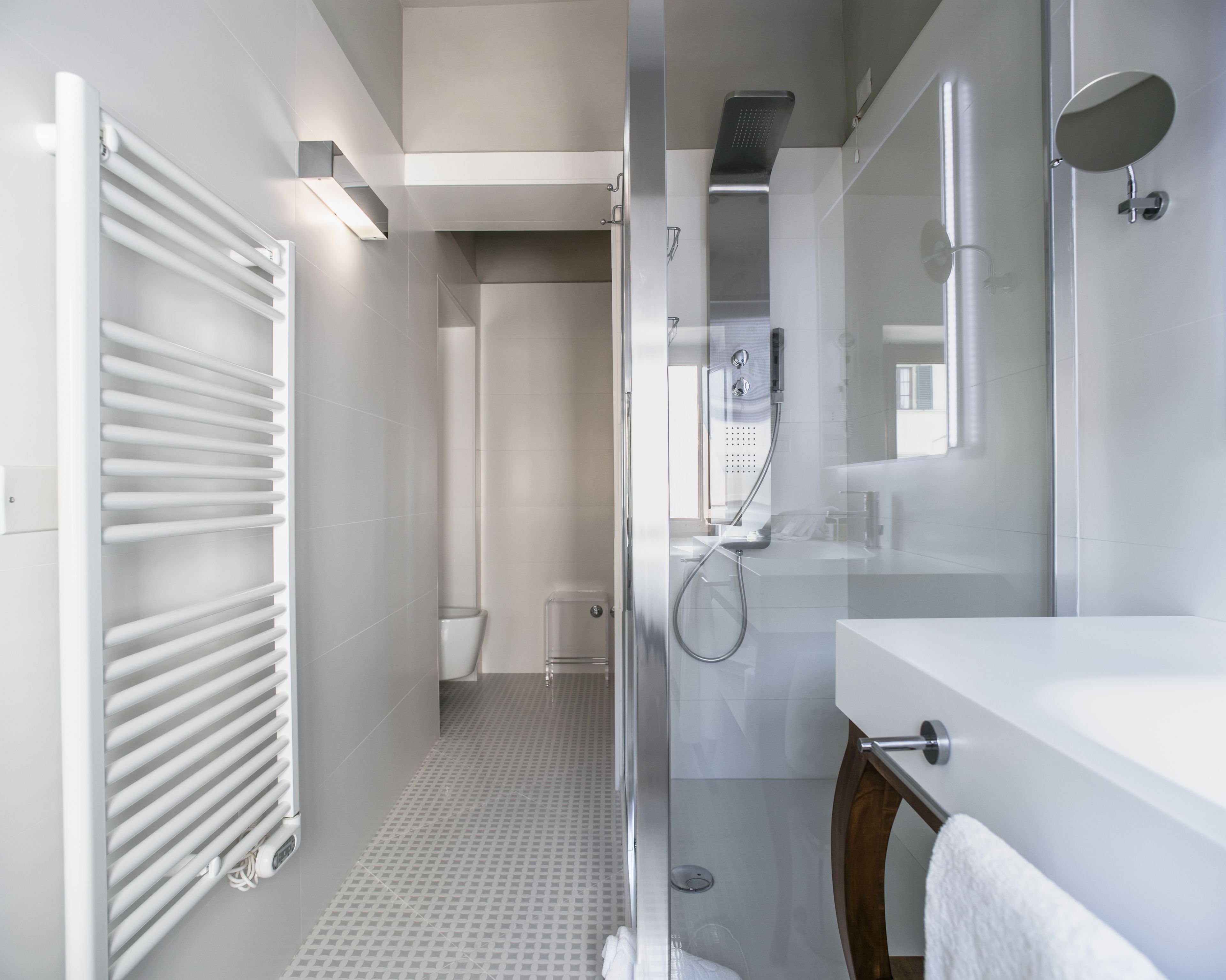 A modern bathroom with a glass shower enclosure, a white sink, and a towel rack.