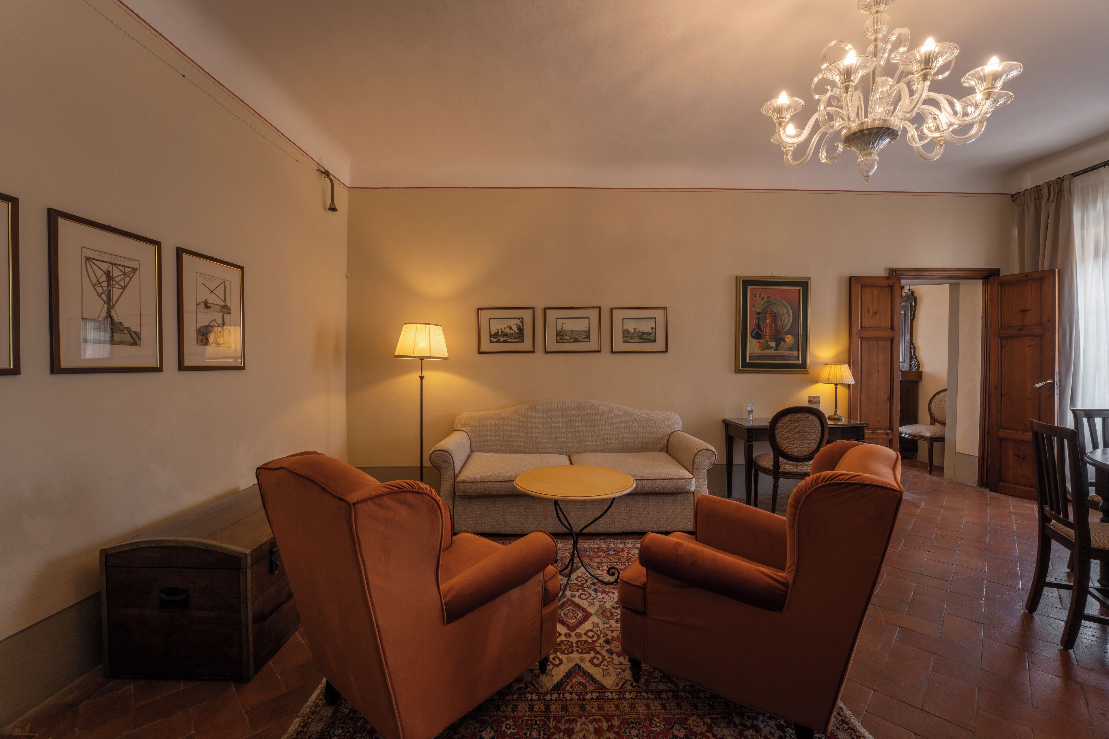 A living room with a sofa, two armchairs, a small round table, a chandelier, and framed pictures on the wall.