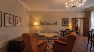 A living room with a sofa, two armchairs, a small round table, a chandelier, and framed pictures on the wall.