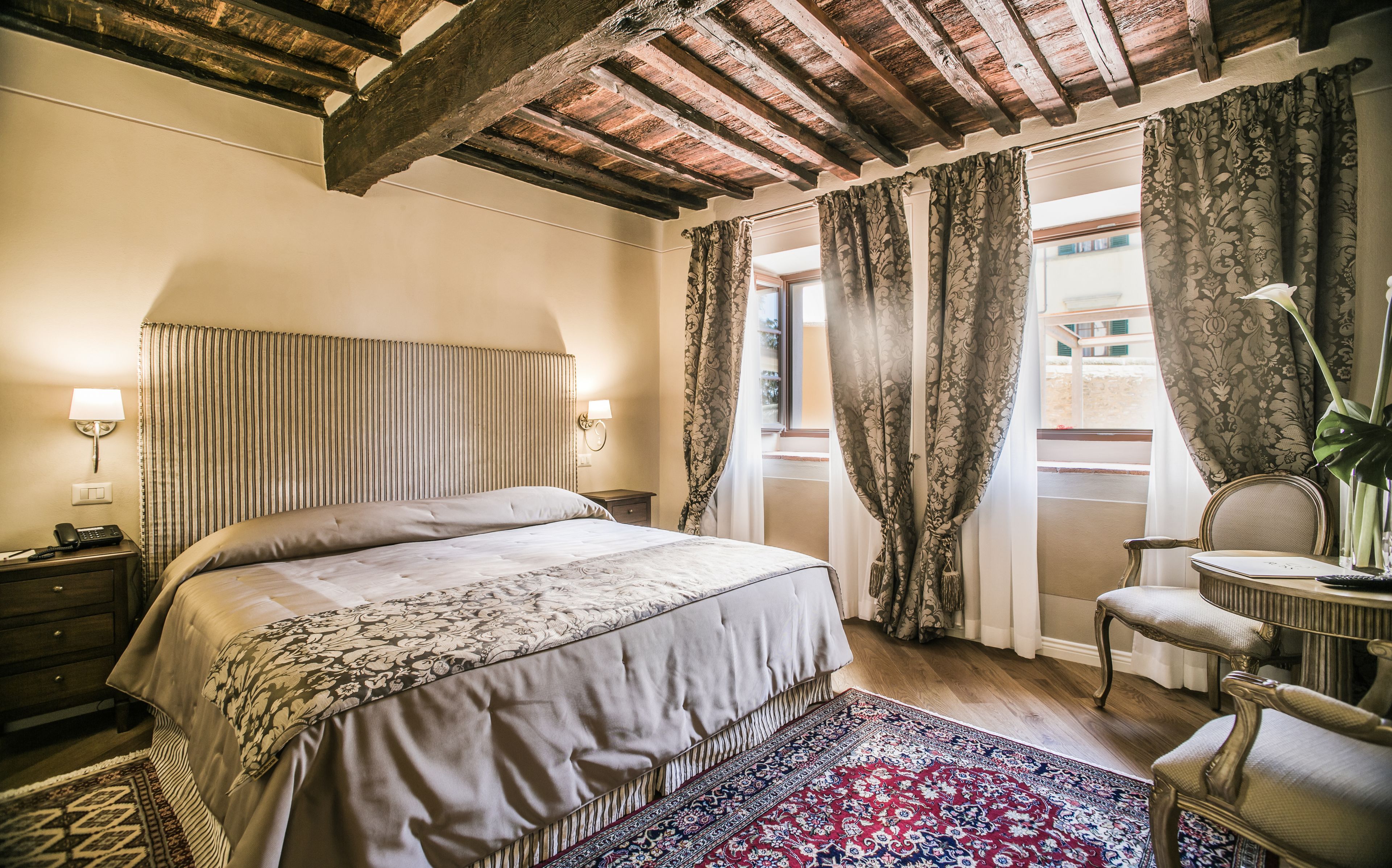 A bedroom with a large bed, a nightstand, a lamp, a chair, and a window with curtains.