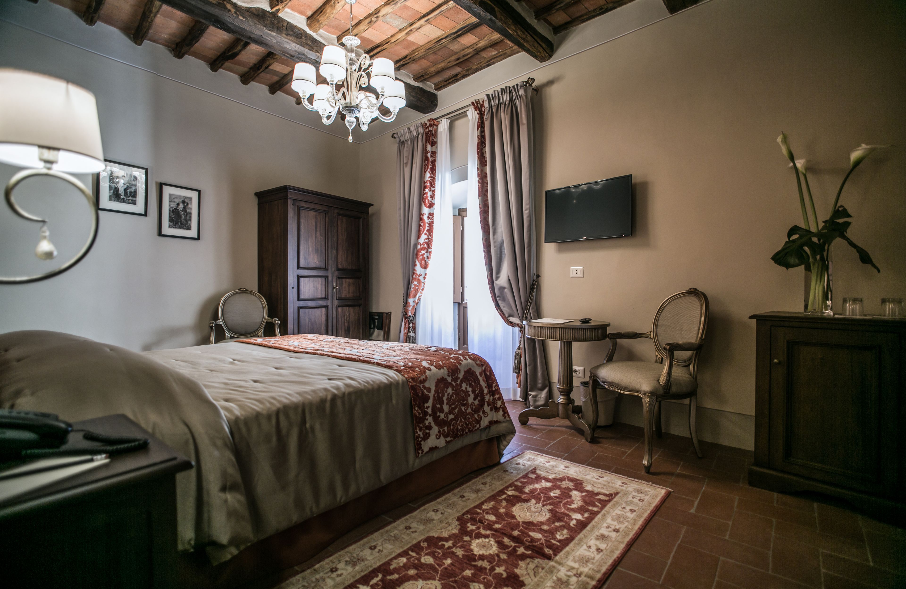 A bedroom with a bed, a desk, a chair, a TV, and a chandelier.