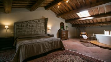 A bedroom with a large bed, a wooden dresser, a chair, a nightstand, a lamp, a mirror, a window, and a skylight.