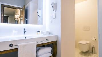 A modern bathroom with a large mirror, white sink, and a hairdryer mounted on the wall.