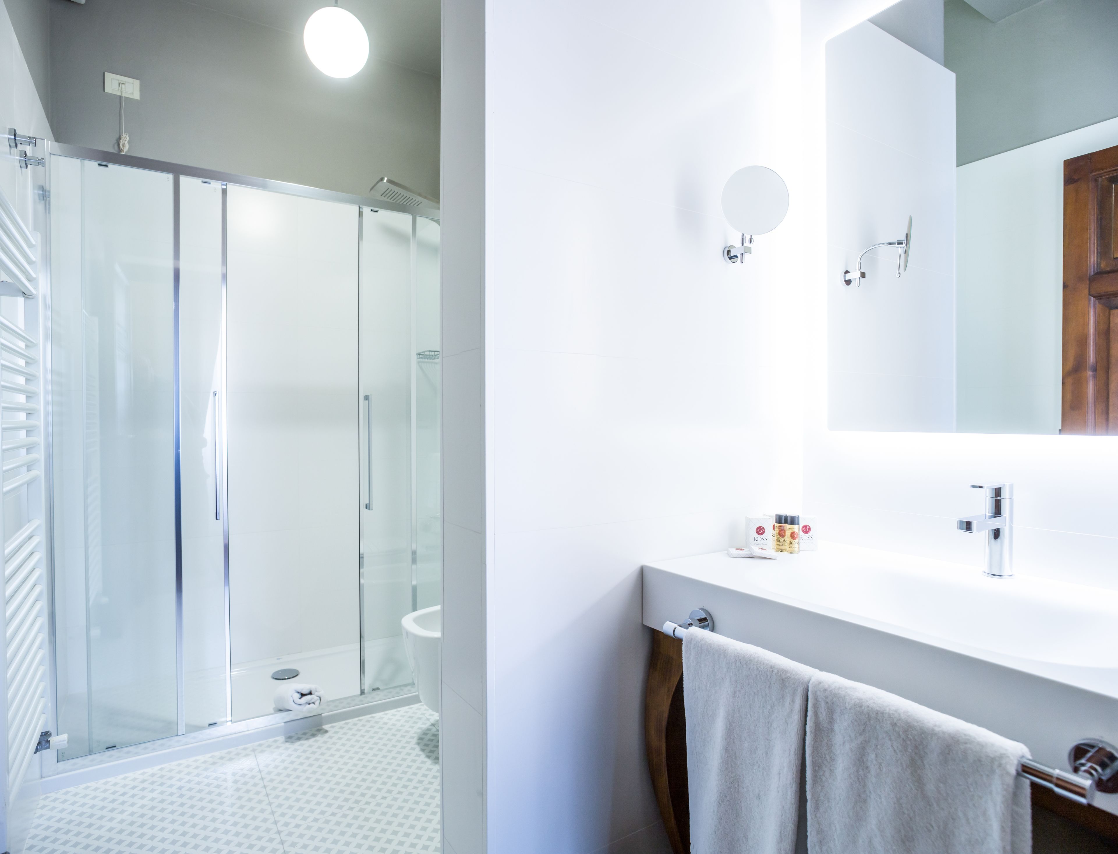 A modern bathroom with a glass shower enclosure, a white sink with a mirror, and a towel rack.