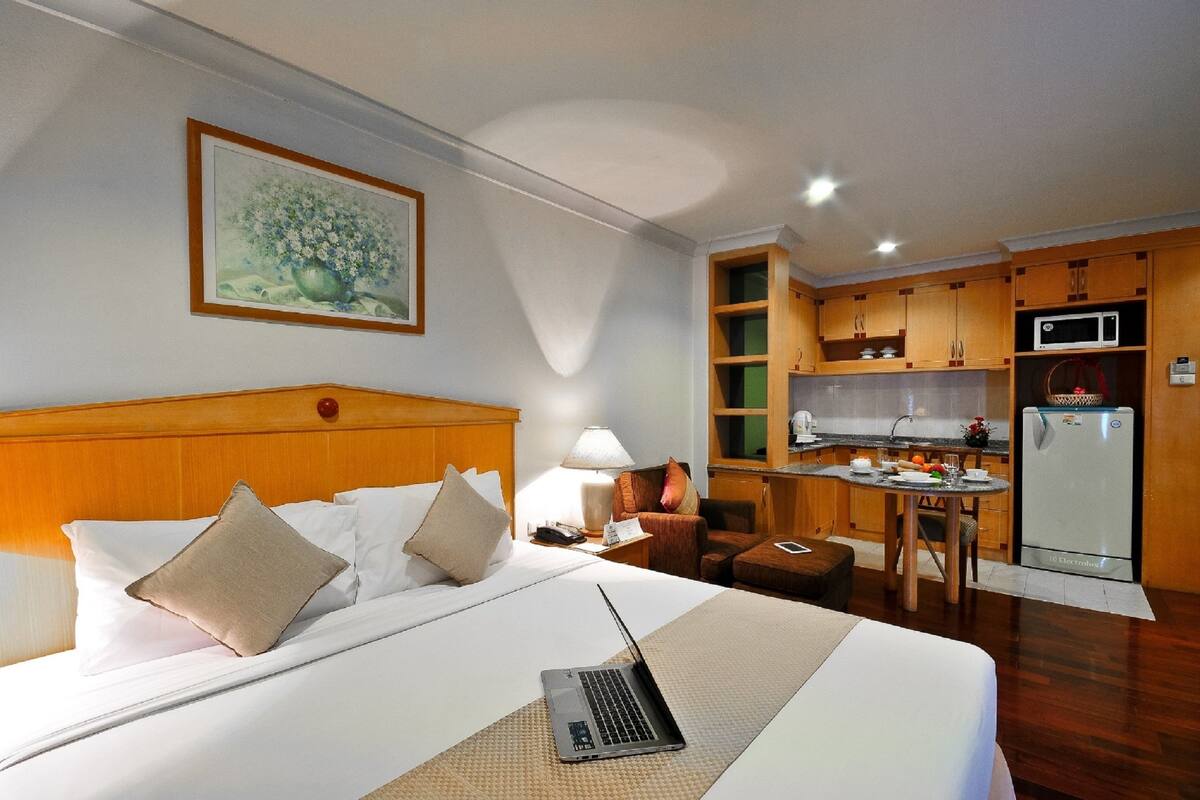 A hotel room with a bed, a laptop on the bed, a small dining table with chairs, a microwave, and a refrigerator.