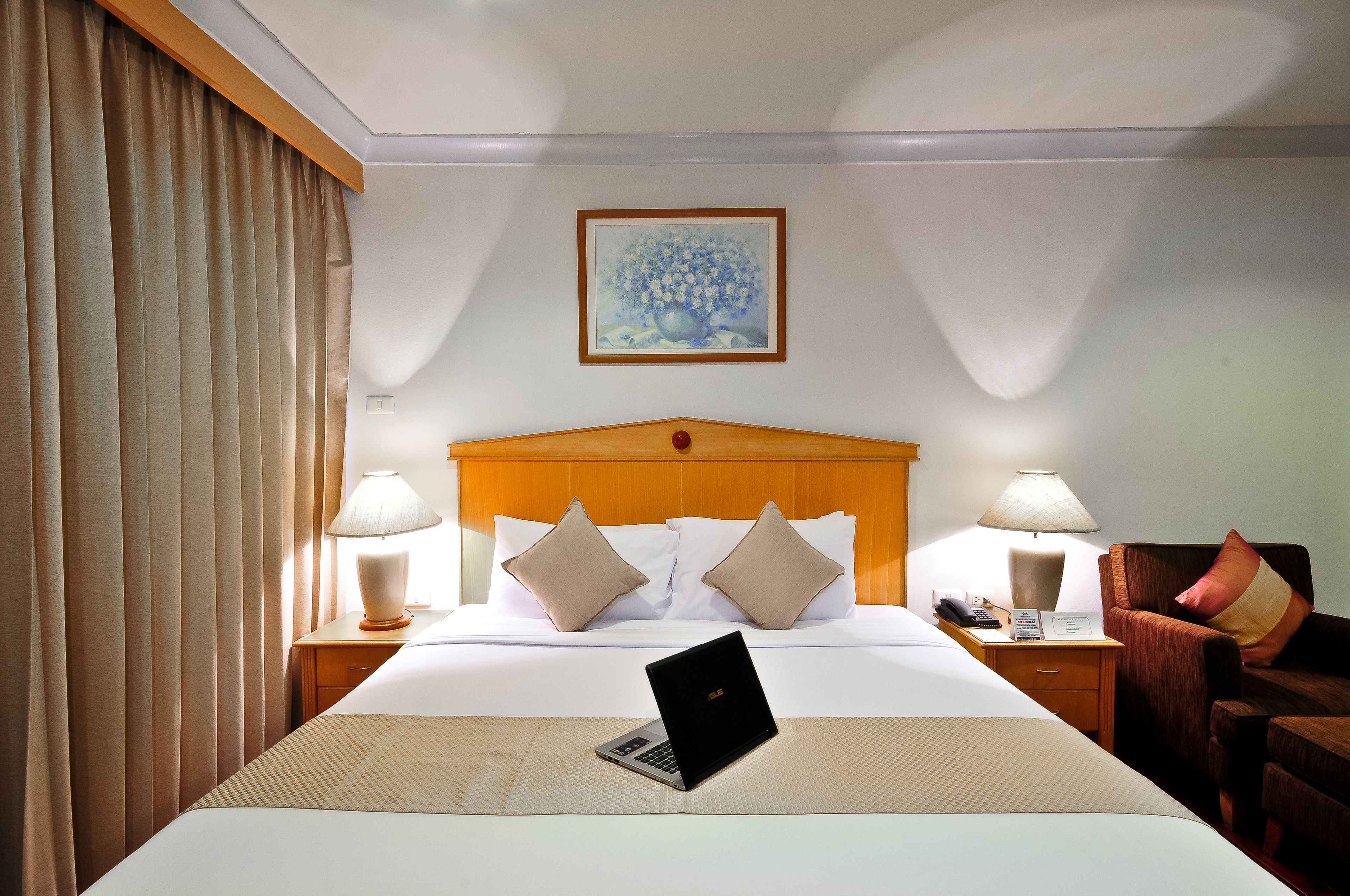 A hotel room with a bed, two bedside tables, a laptop, a lamp, and a chair.