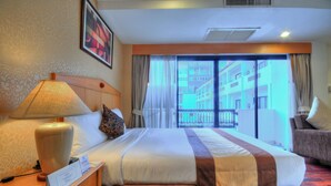 Habitación de hotel con una cama grande, una mesita de noche con lámpara, una silla y vista a un edificio a través de la ventana.