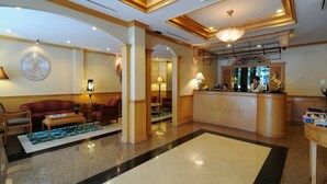 Vestíbulo de hotel con mostrador de recepción, zona de estar con sofás y sillones, y una pared decorativa.