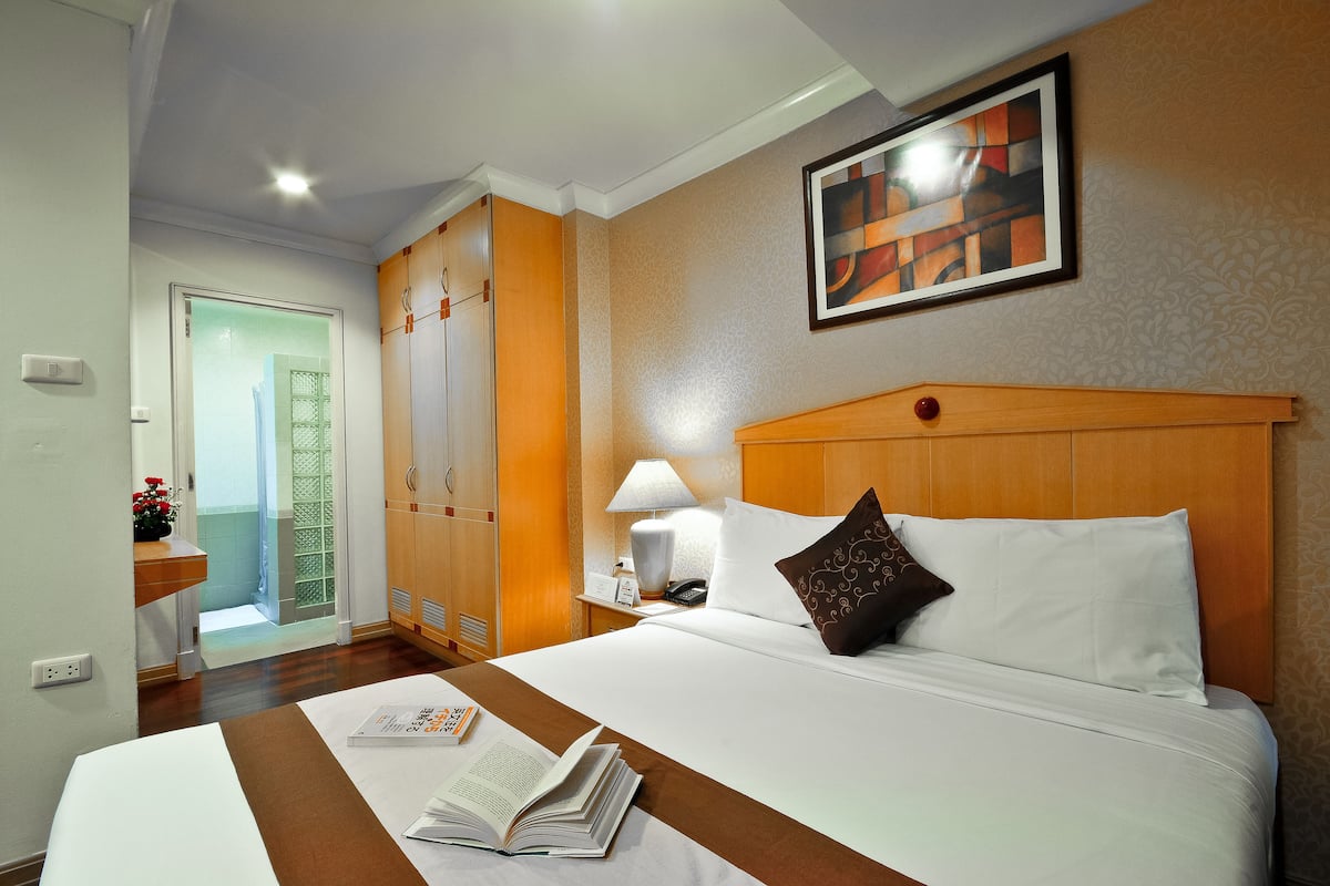 A hotel room with a bed, a nightstand, a lamp, a painting, and a door leading to a bathroom.