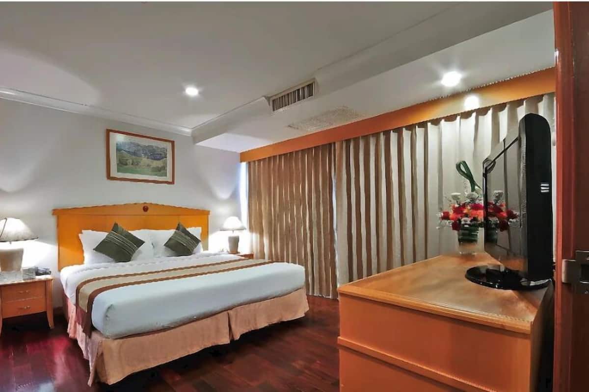 A hotel room with a large bed, two bedside tables with lamps, a wooden headboard, a painting on the wall, a mirror, and a curtain.