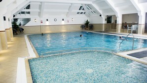 An indoor swimming pool with a tiled floor, a diving board, and a seating area with chairs and tables. - Crown Hotel (Carlisle)