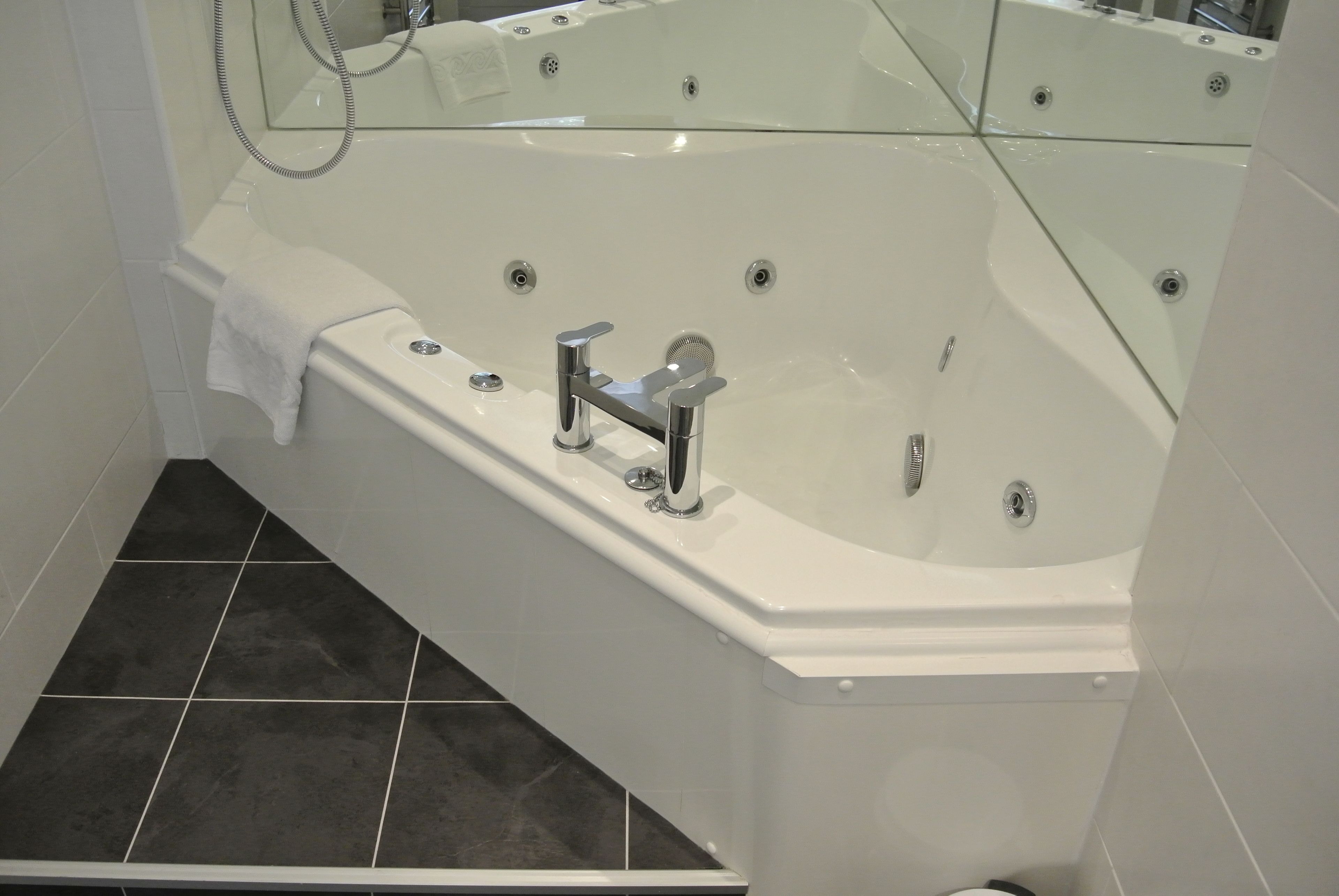 A modern bathroom with a large bathtub, a handheld showerhead, and a towel rack.