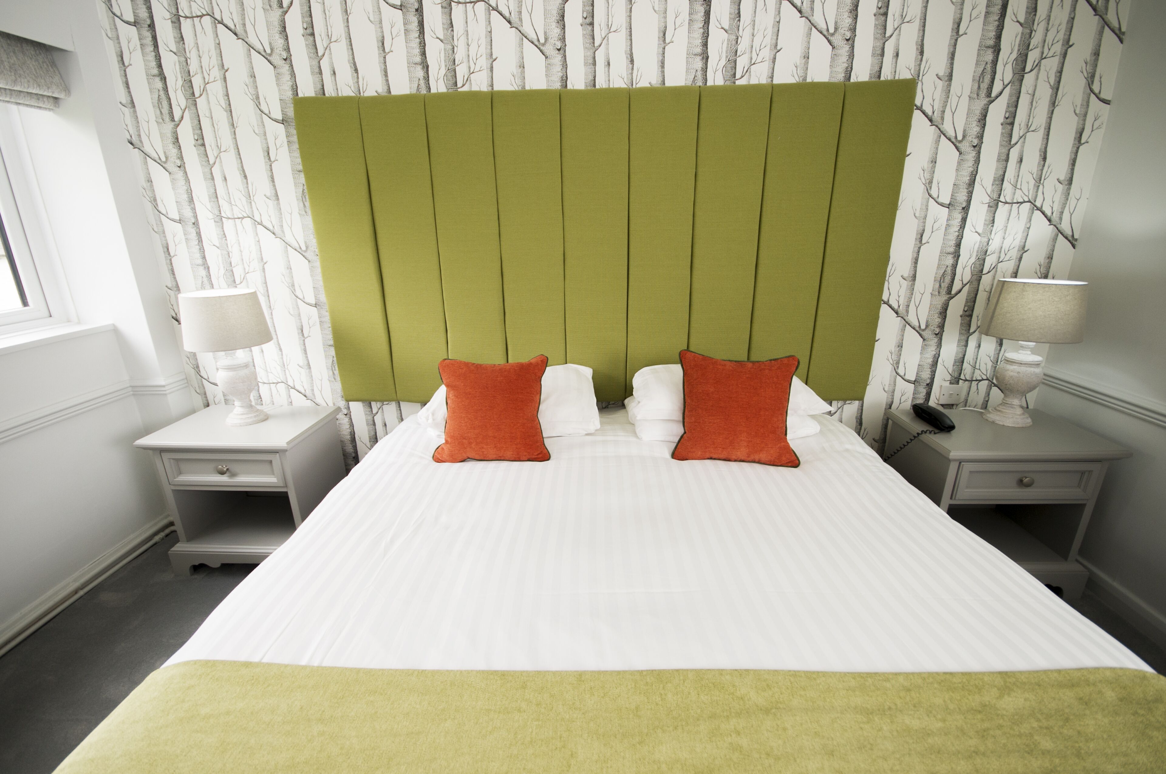 Una habitación de hotel con una cama grande, dos mesitas de noche y un cabecero verde.