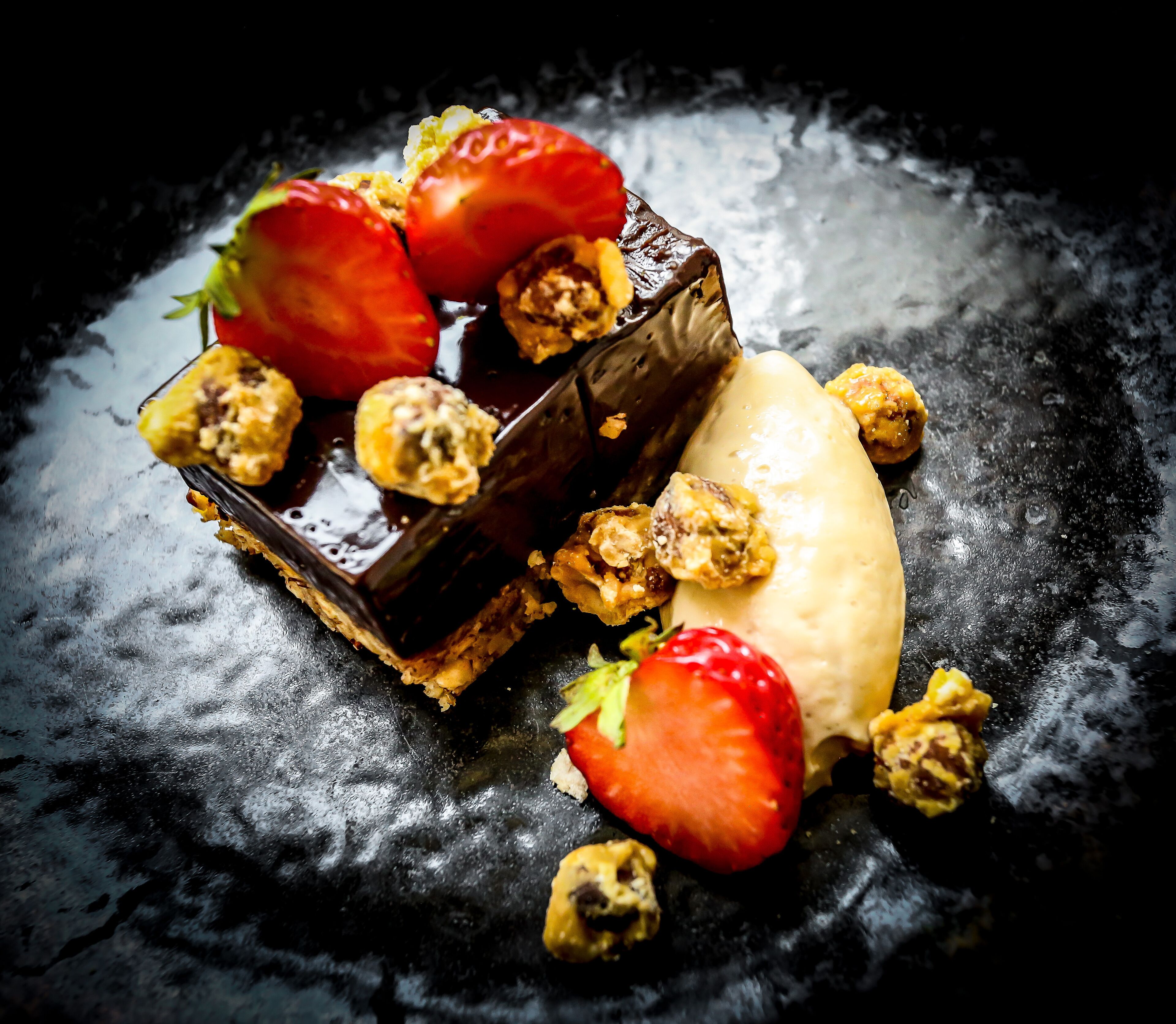 Dessert met aardbeien, chocolade en noten op een donker bord.
