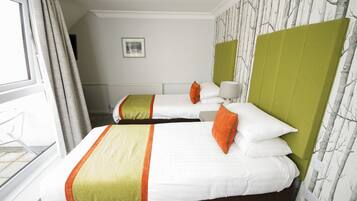 A hotel room with two beds, each with white bedding and orange pillows, green headboards, and a window with curtains.